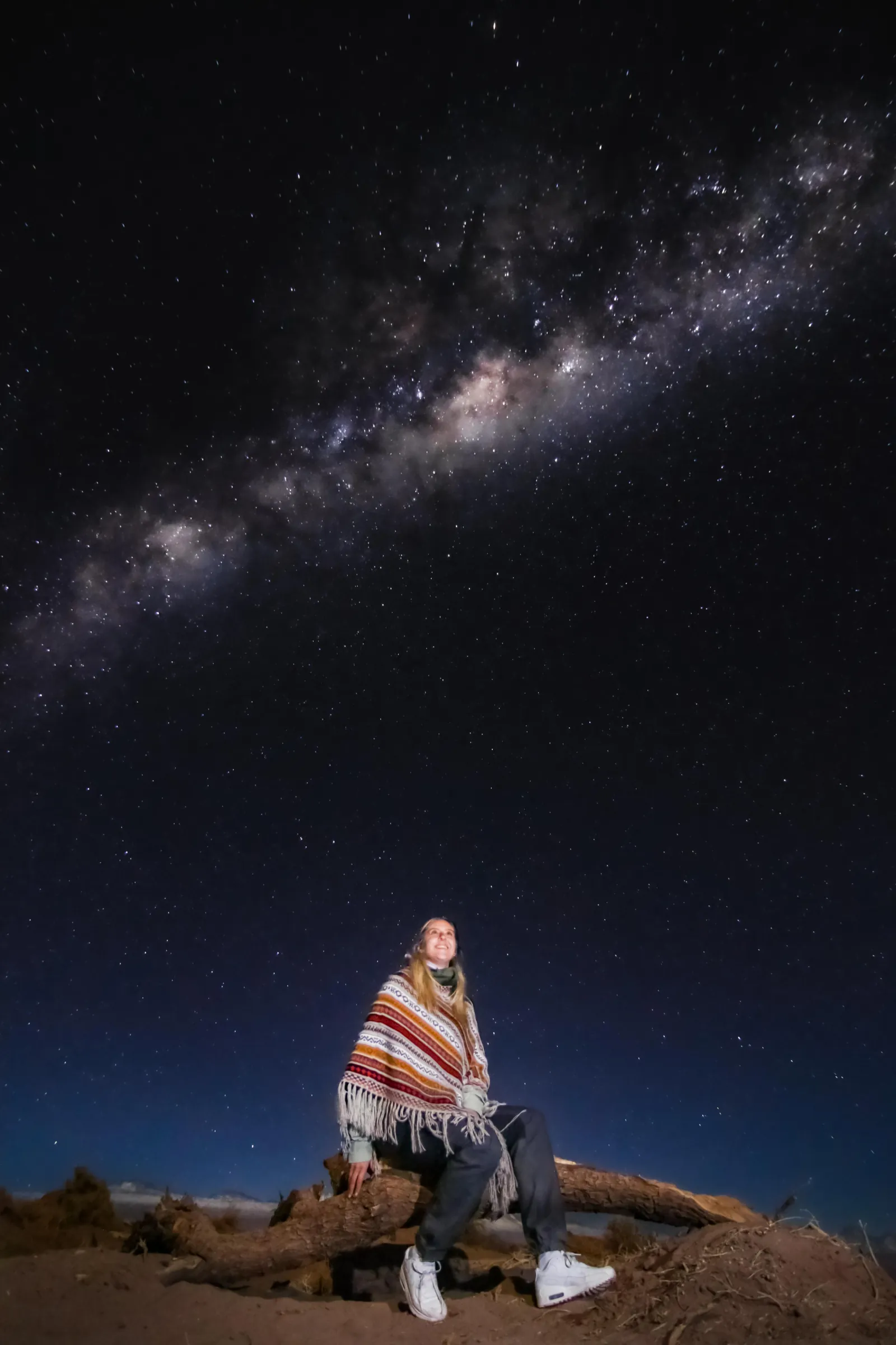 A traveller in a striped poncho sits under the Milky Way on a stargazing night