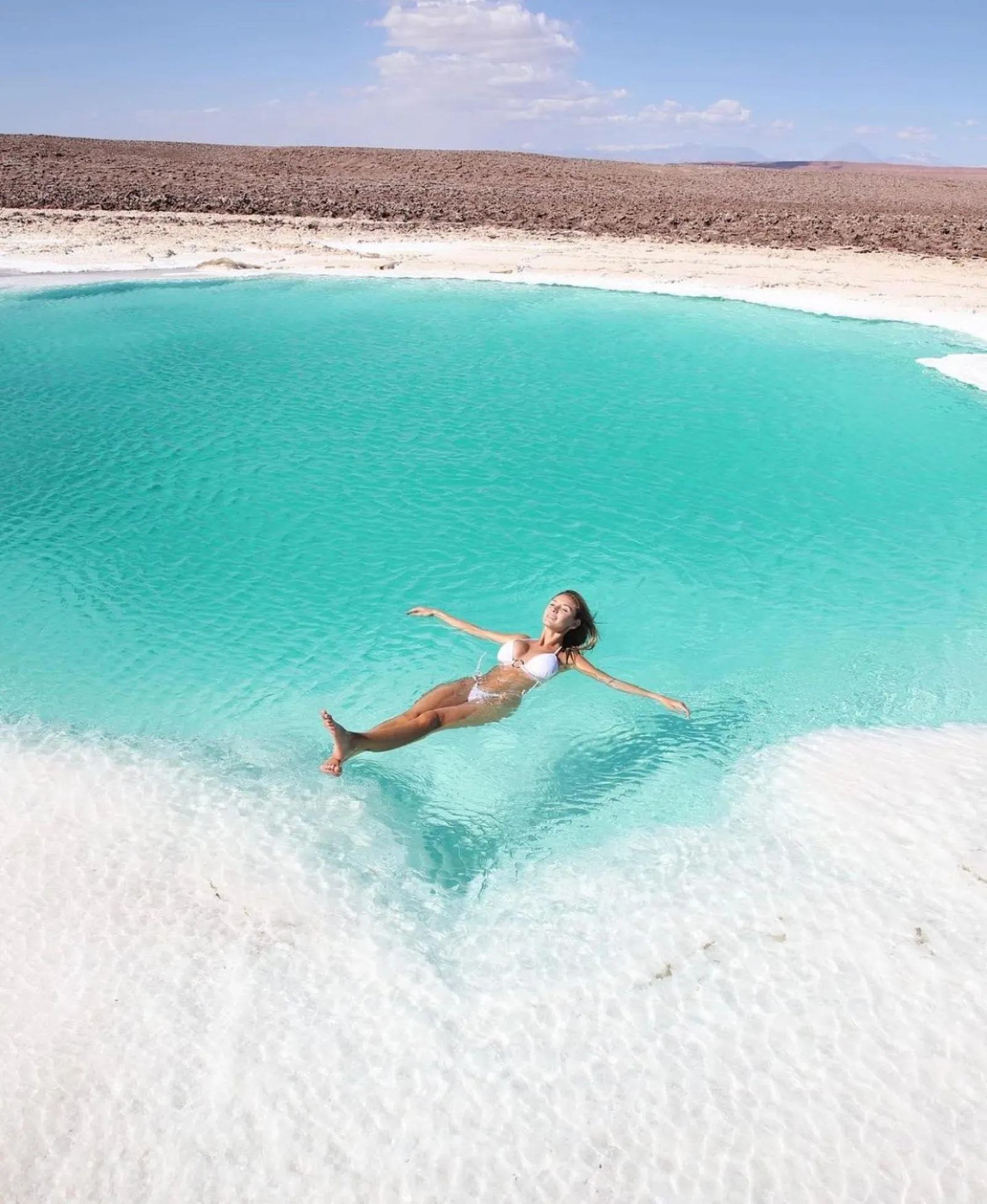 A woman floats on her back in a turquoise lagoon edged with white salt