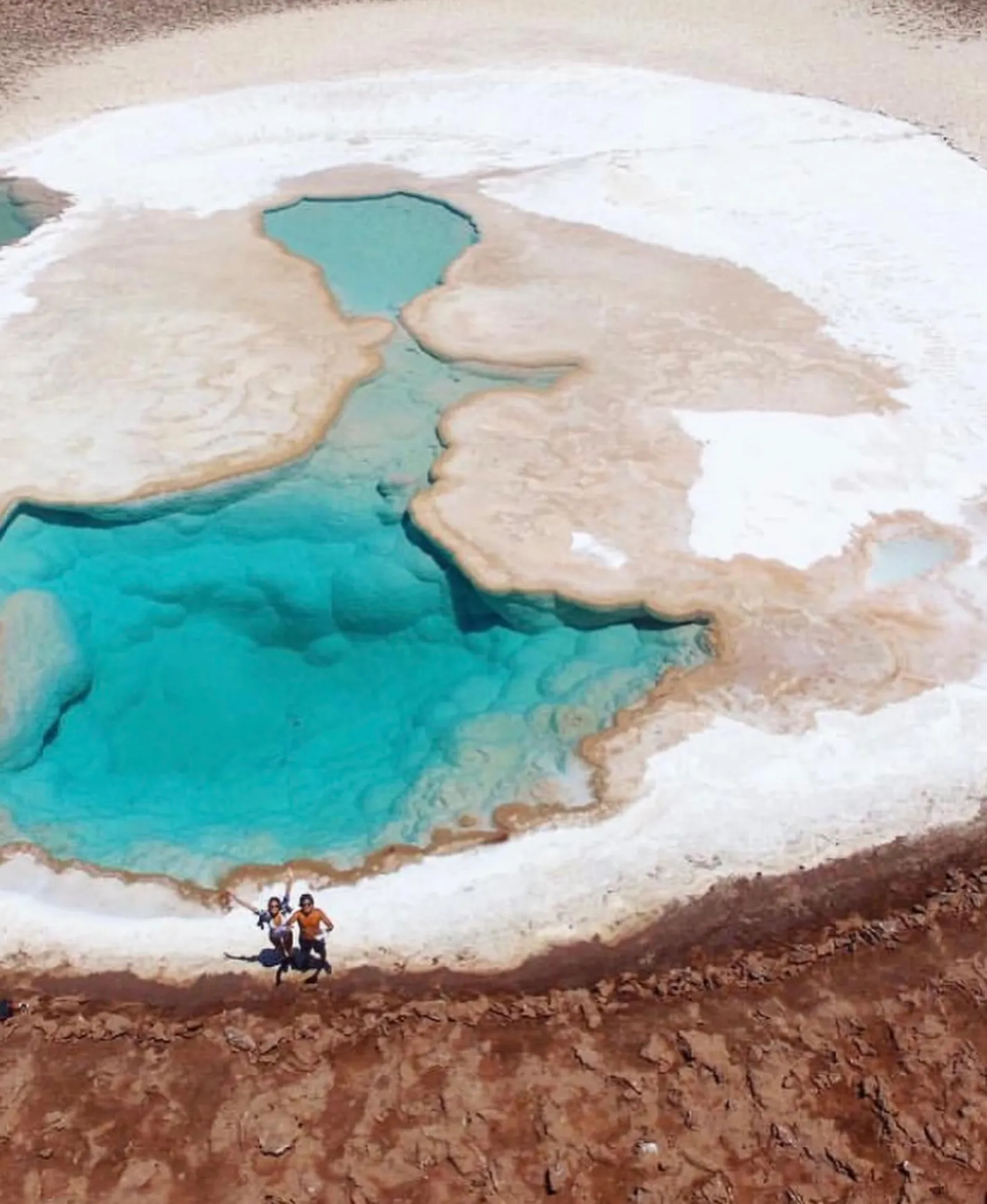 Aerial view of turquoise salt lagoons with two people standing on the white shore