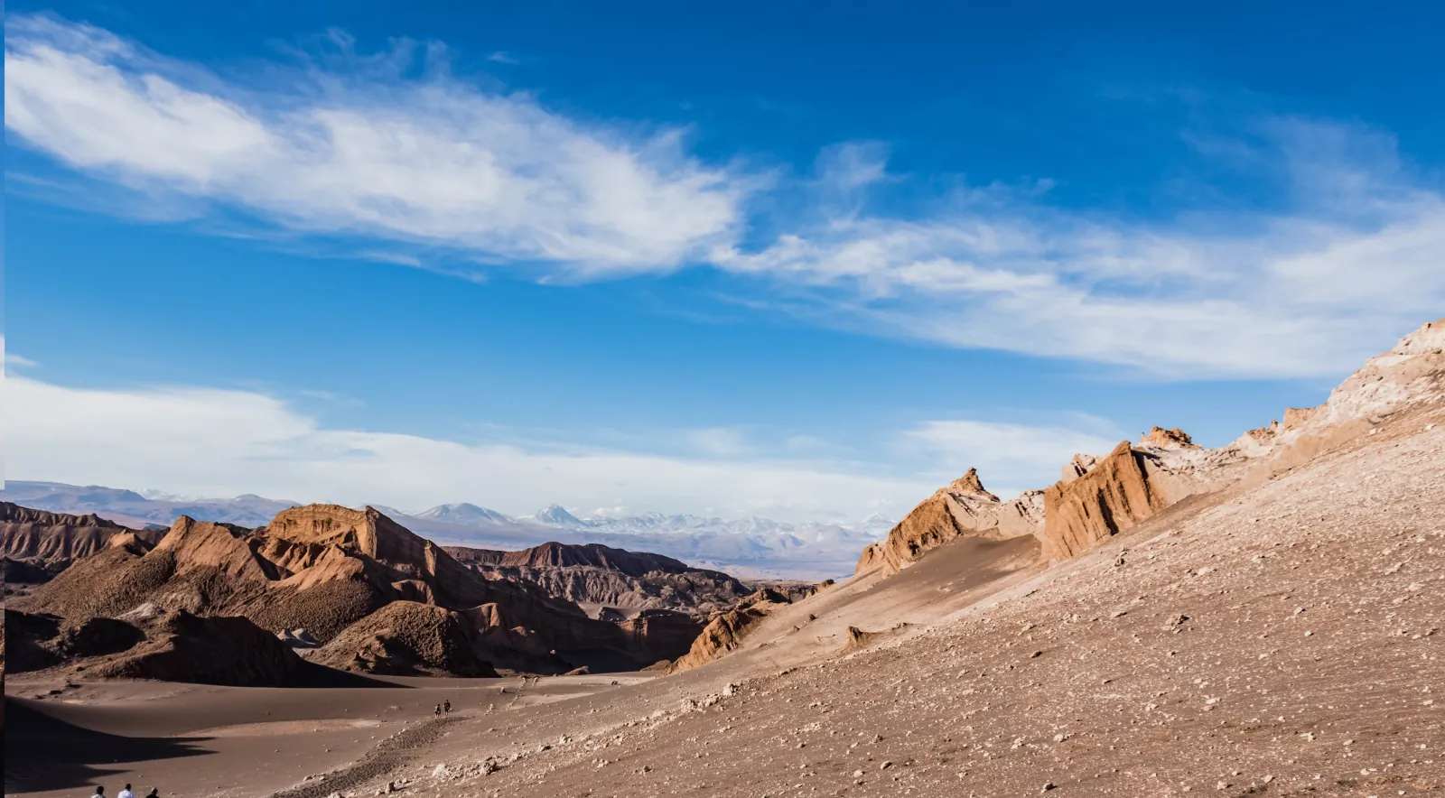 Sandy slopes and jagged rock crests in Valle de la Luna under a cloud-streaked sky