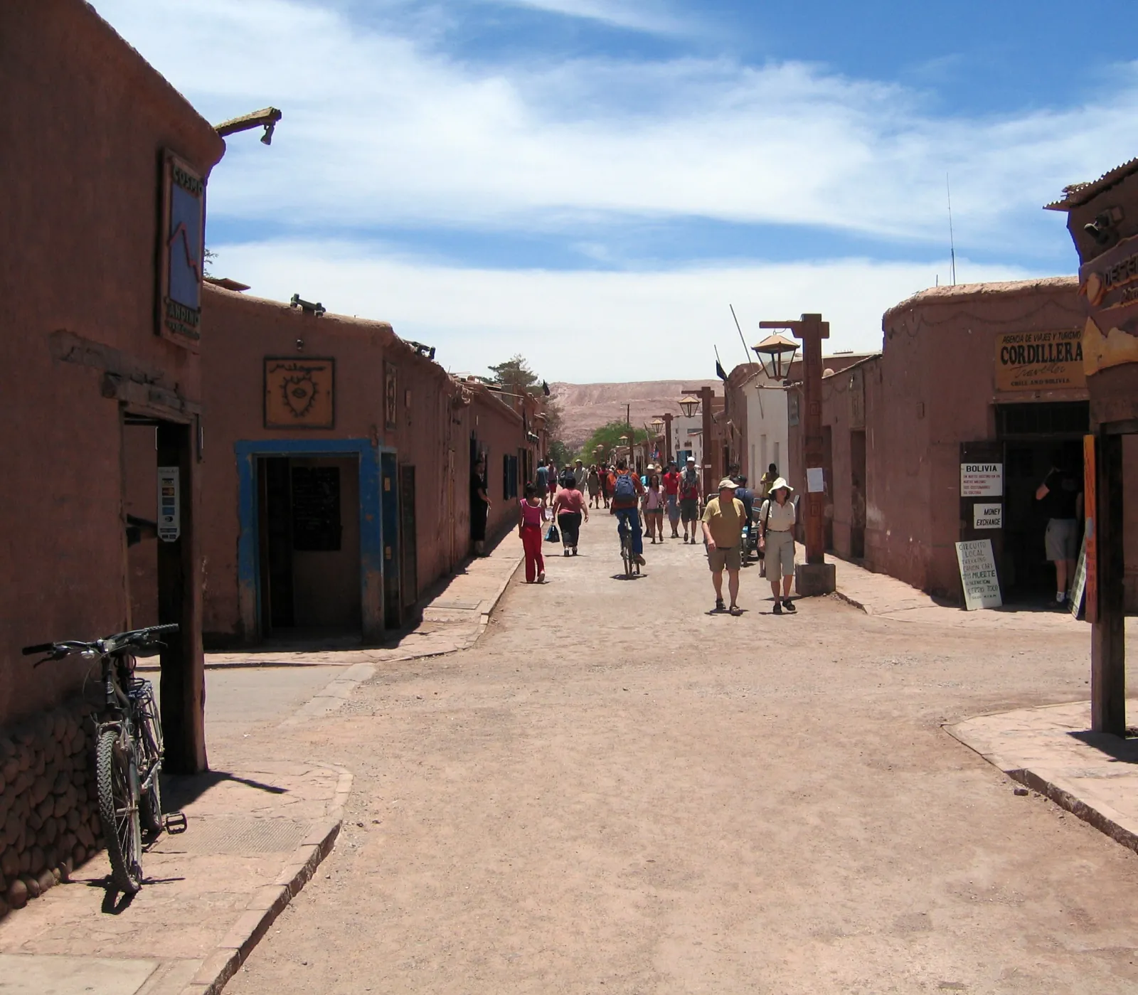 Adobe buildings line a dirt street in central San Pedro de Atacama, with walkers and a parked bicycle