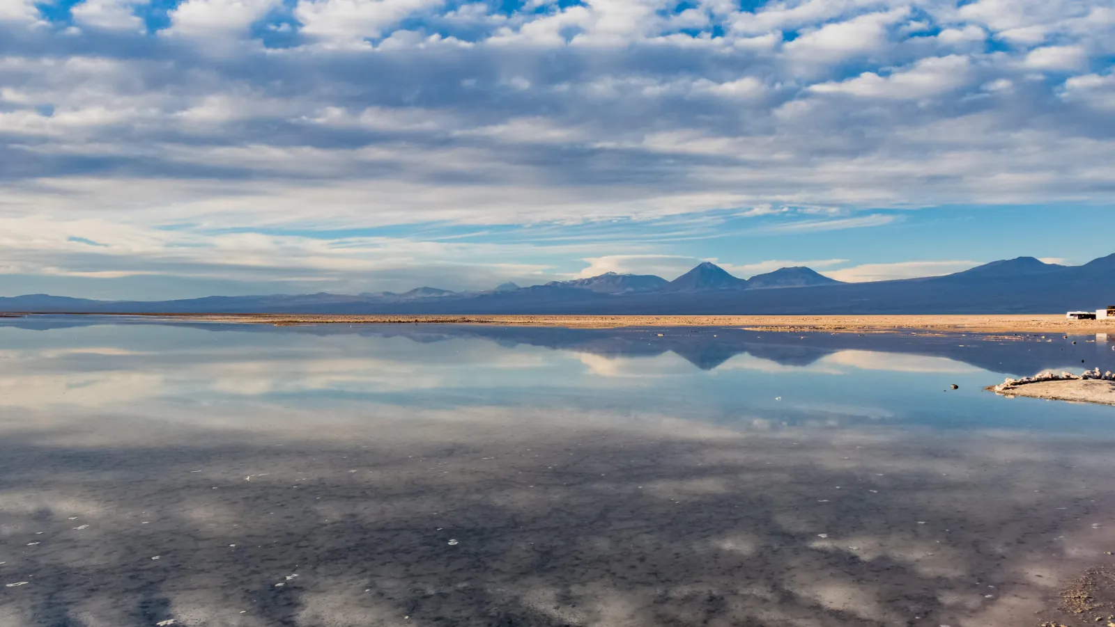 Clouds and distant mountains mirrored in a calm lagoon on the Salar de Atacama