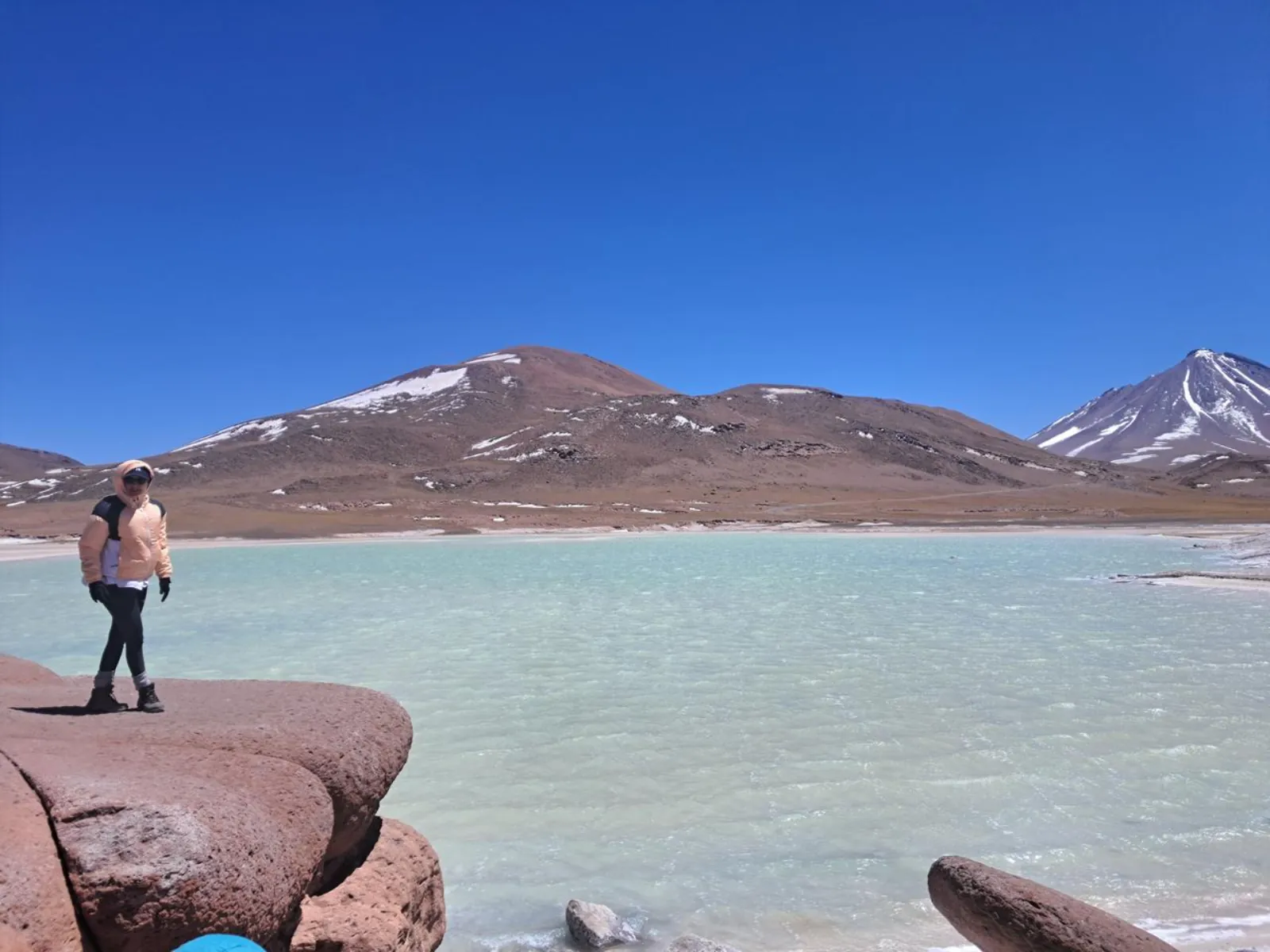 A traveler on red rocks beside a turquoise lagoon at Piedras Rojas