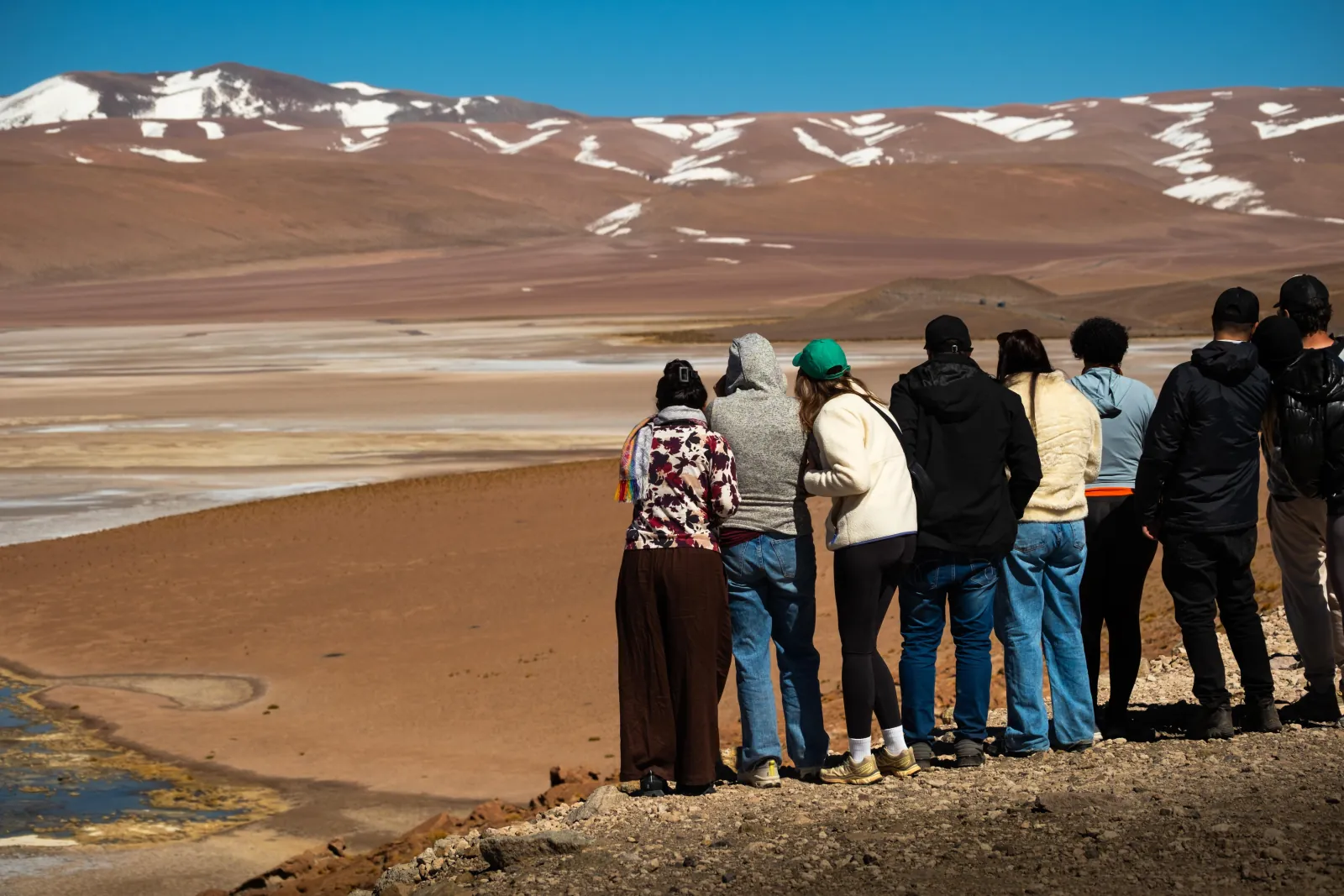 A tour group looks out over a salt flat and snow-patched hills