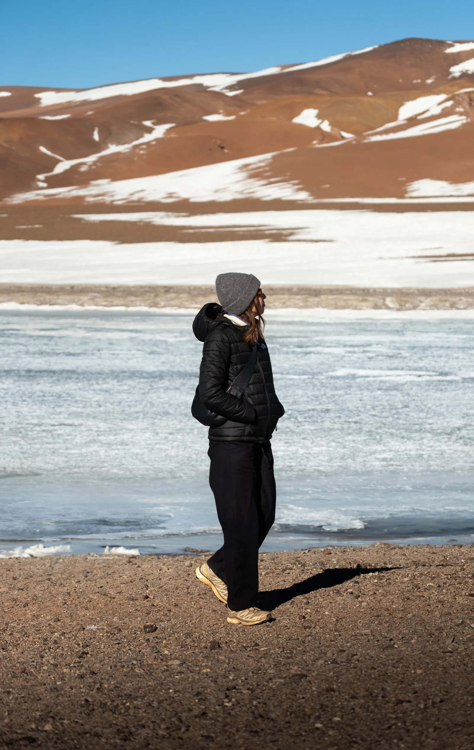 A traveller in a beanie stands at the icy edge of a high-altitude lagoon