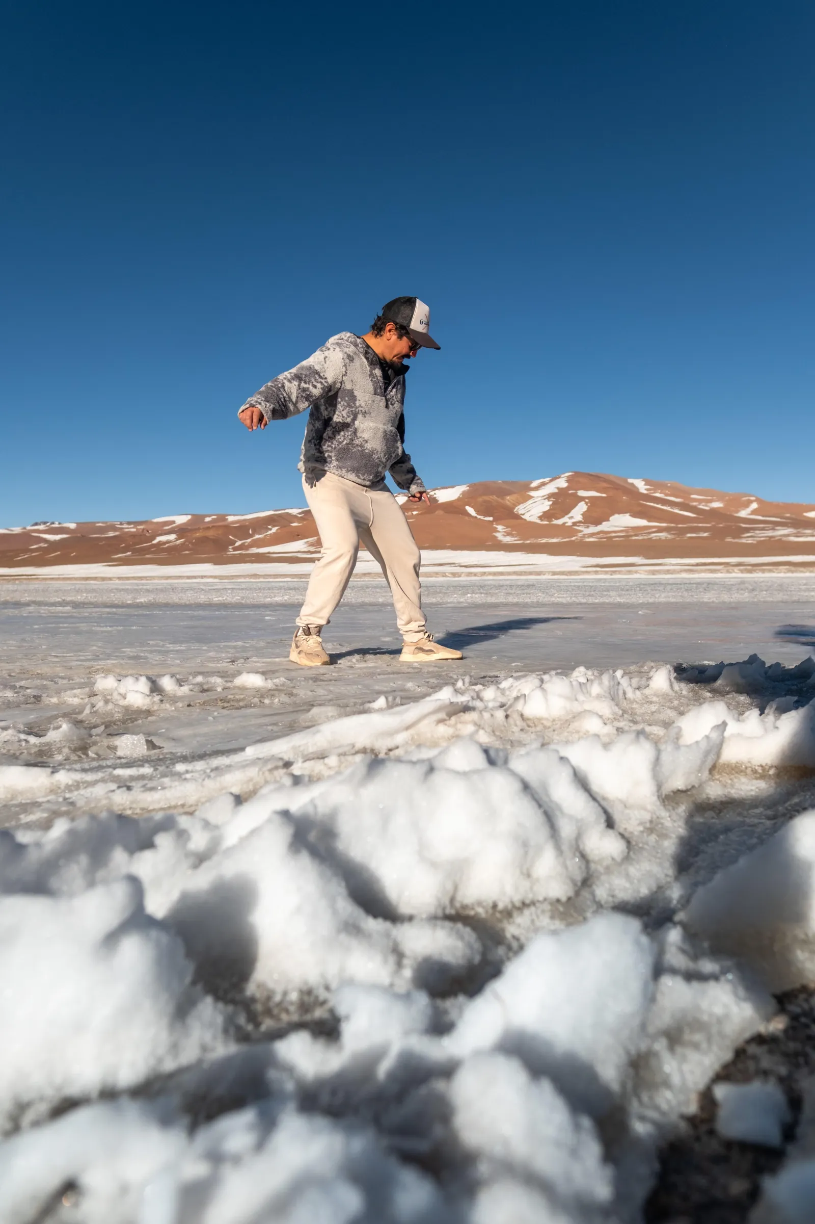 A traveller steps across snow and salt crust on a high-altitude salt flat