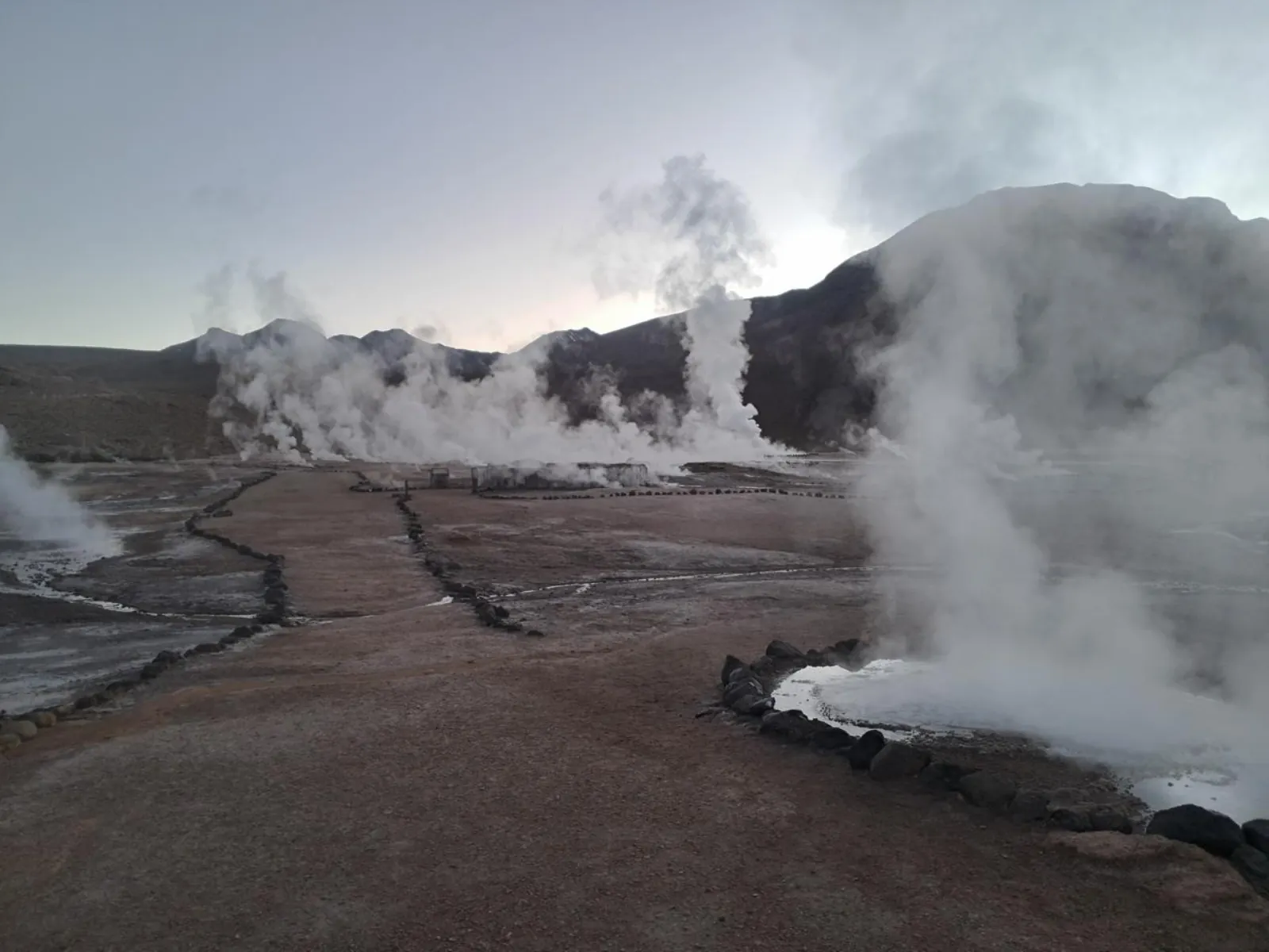 Steam drifts across a stone-edged path at El Tatio in early morning light
