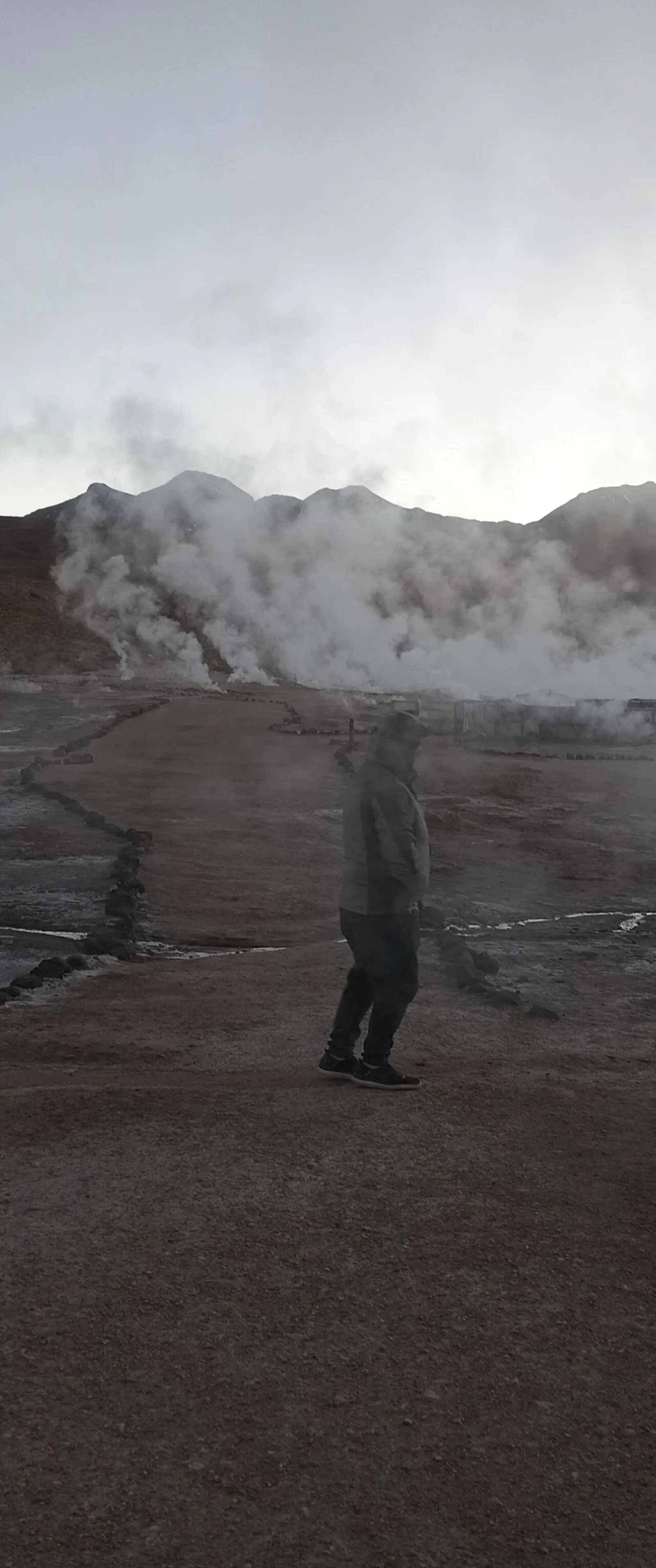 A visitor stands among drifting steam on the El Tatio field at dawn