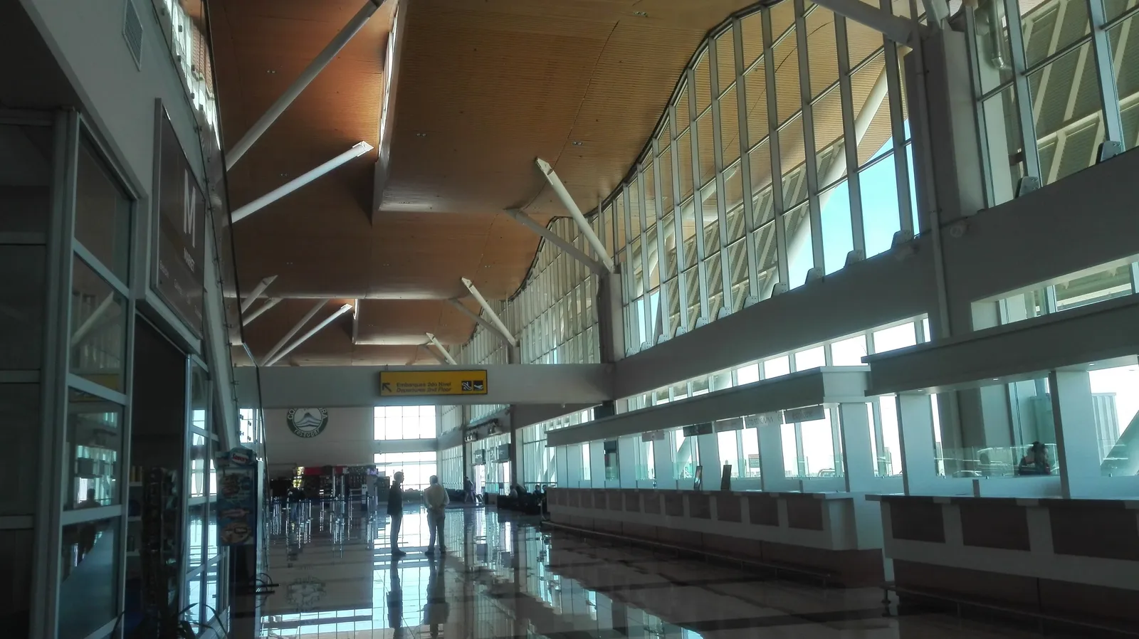 A long glass-walled hall under a timber ceiling inside the El Loa Airport terminal in Calama