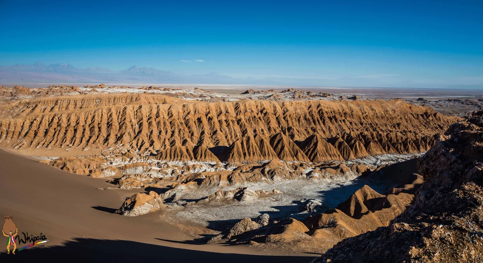 Rows of eroded ridges and a long sand slope in Valle de la Luna under a deep blue sky