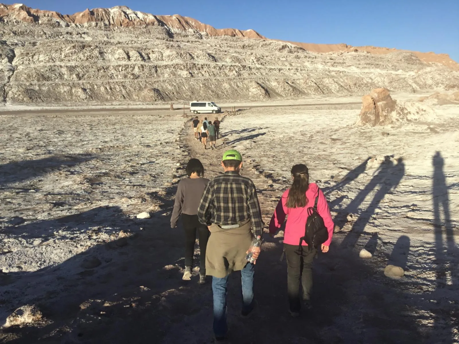 Travellers walk across salt-crusted ground toward a parked white van in Valle de la Luna