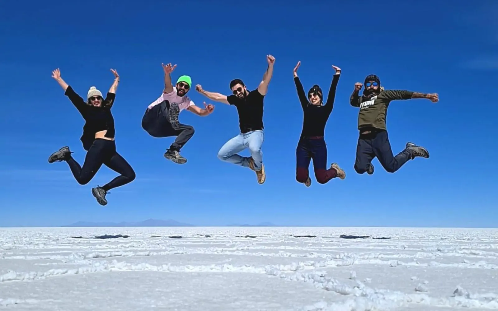 Five travellers leap into the air above the white Salar de Uyuni