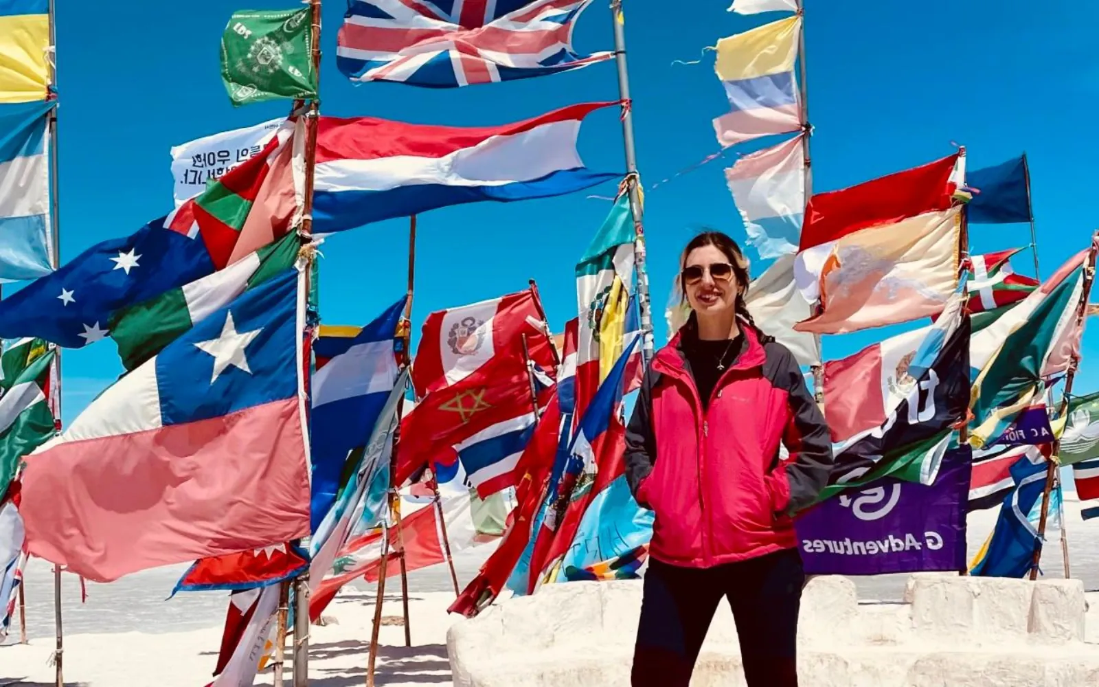 A traveller in a pink jacket stands among national flags at the Plaza de las Banderas